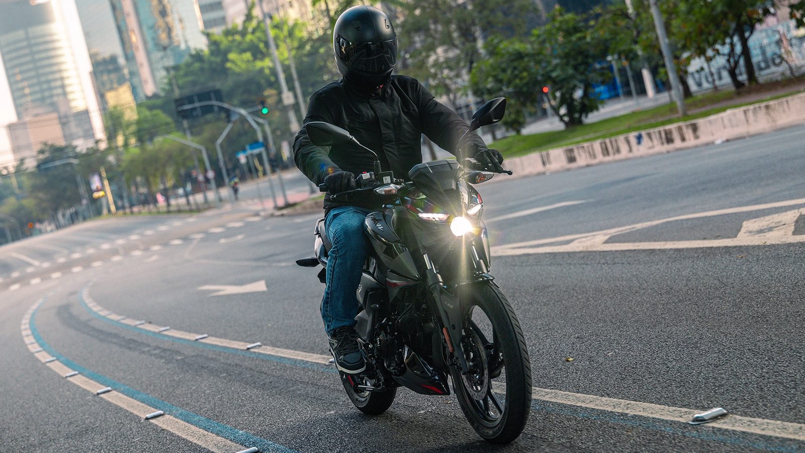 Motociclista pilotando a Bajaj Pulsar N150 preta em avenida de São Paulo, iluminação do farol acesa